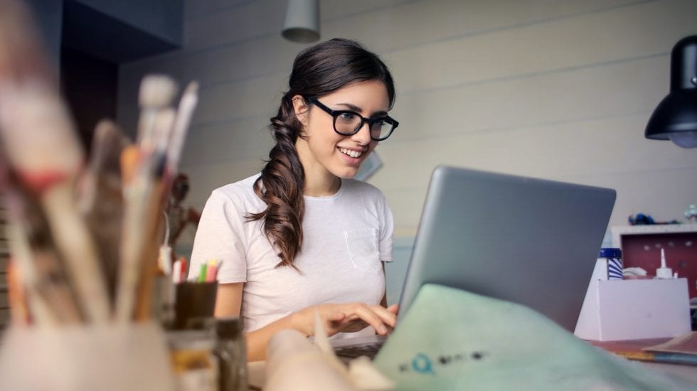 Chica trabajando en un ordenador, cómodamente en su casa. Teletrabajo.